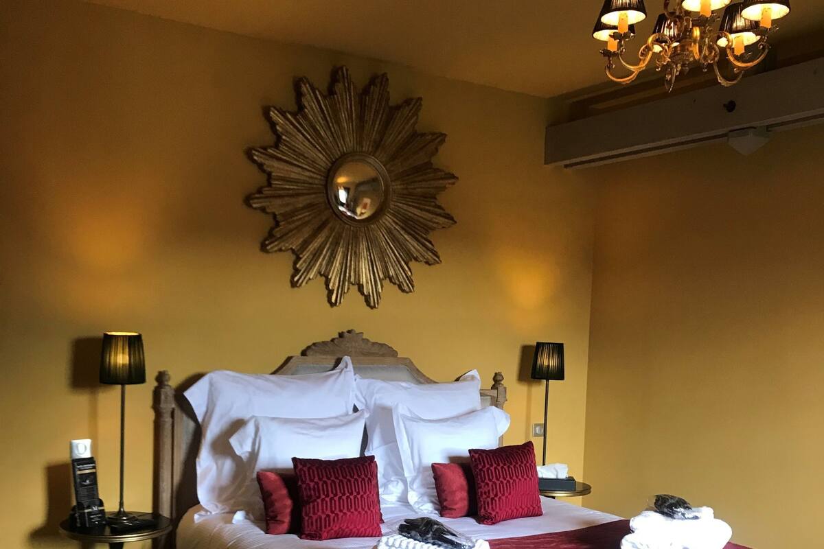 Een hotelkamer met een groot bed, een houten vloer, een kroonluchter en een spiegel aan de muur.