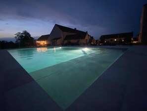 Une piscine au design géométrique, entourée de bâtiments dont l’éclairage est chaleureux.