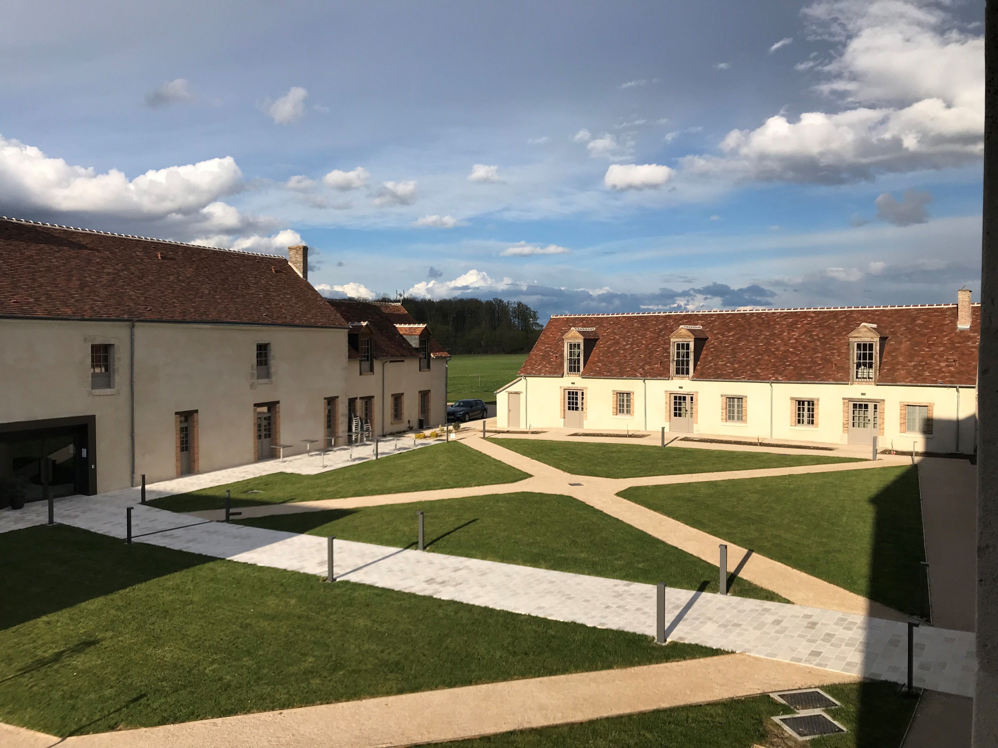A courtyard with two-story buildings, a paved walkway, and a grassy area.
