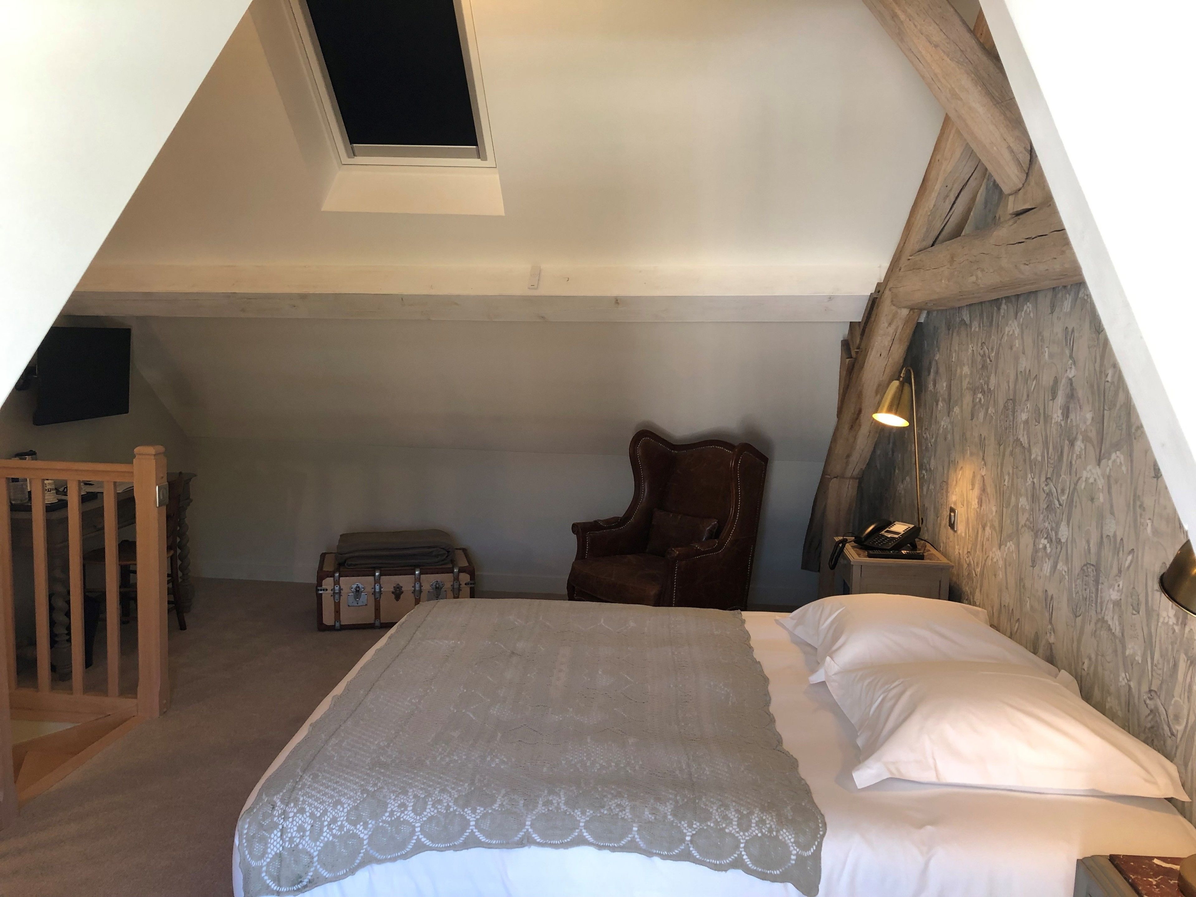 A bedroom with a bed, a chair, a small table, and a window.