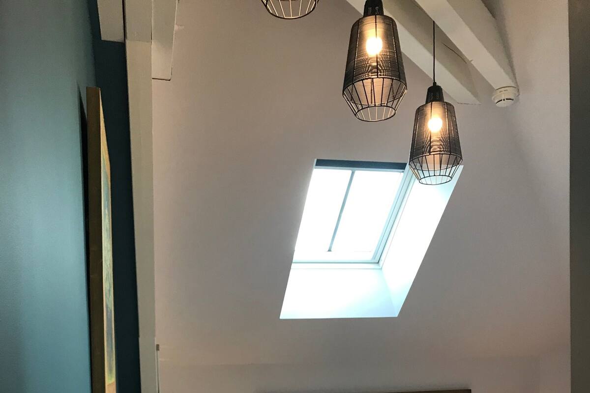 Een slaapkamer met dakraam, een bed met turquoise kussens en hanglampen.