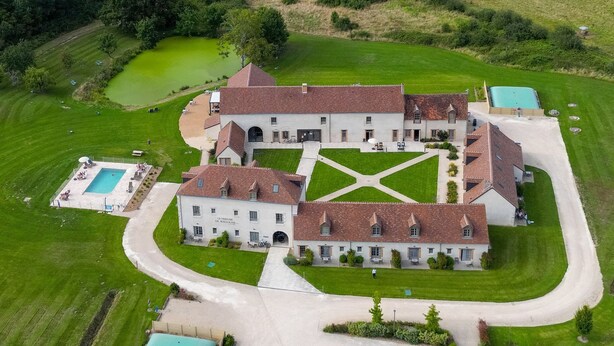 Ein großes, mehrgeschossiges Gebäude mit einem symmetrischen Innenhof, umgeben von üppiger Bepflanzung und einem kleinen Teich.