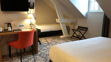 A hotel room with a desk, a red chair, a bed, a small table, and a window.