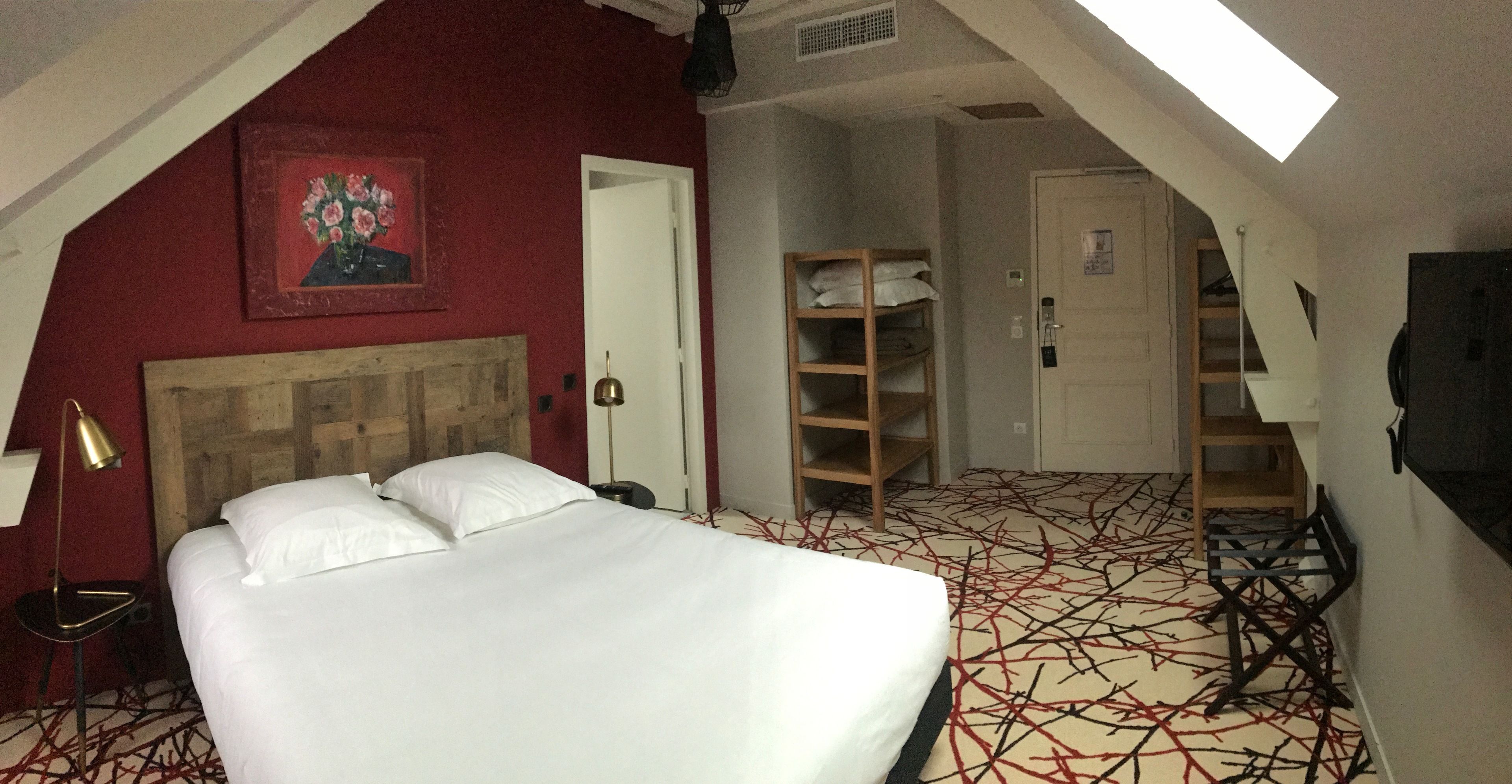 A hotel room with a bed, a desk, a chair, a wardrobe, and a painting on the wall.