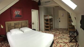 Une chambre d’hôtel avec un lit, un bureau, une chaise, une armoire et un tableau au mur.