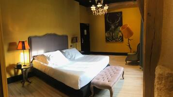 Un dormitorio con una cama grande, una mesita de noche con lámpara, un banco, una araña y un cuadro de un ciervo en la pared.