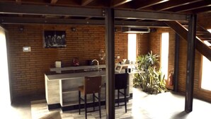 A kitchen with a brick wall, a wooden ceiling, and a bar area with stools. - Boschetto Suites De Bosques (Athos Pampa)