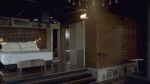A modern bedroom with a brick accent wall, a bed with white linens, and a bench. - Boschetto Suites De Bosques (Athos Pampa)