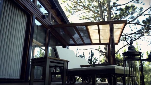 An outdoor seating area with a wooden table and chairs, a covered patio, and a view of trees and a building. - Boschetto Suites De Bosques (Athos Pampa)