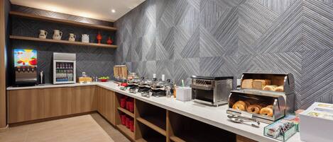 A modern kitchen with a microwave, toaster, and coffee machine. There are shelves with kitchenware and a fruit bowl.