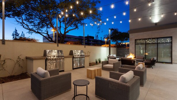 Une terrasse extérieure aménagée avec des meubles en osier, un barbecue et des guirlandes lumineuses.