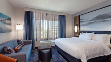 A hotel room with a large bed, a sofa, a small table, and a painting on the wall.