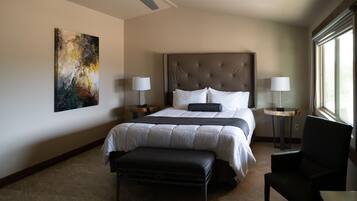 A hotel room with a large bed, a ceiling fan, a painting on the wall, and a window providing natural light.