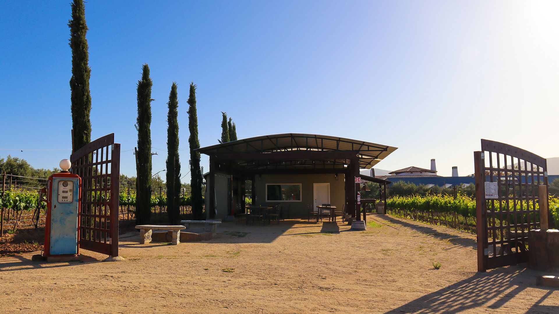 A building with a covered patio, a gate, and a vineyard in the background.