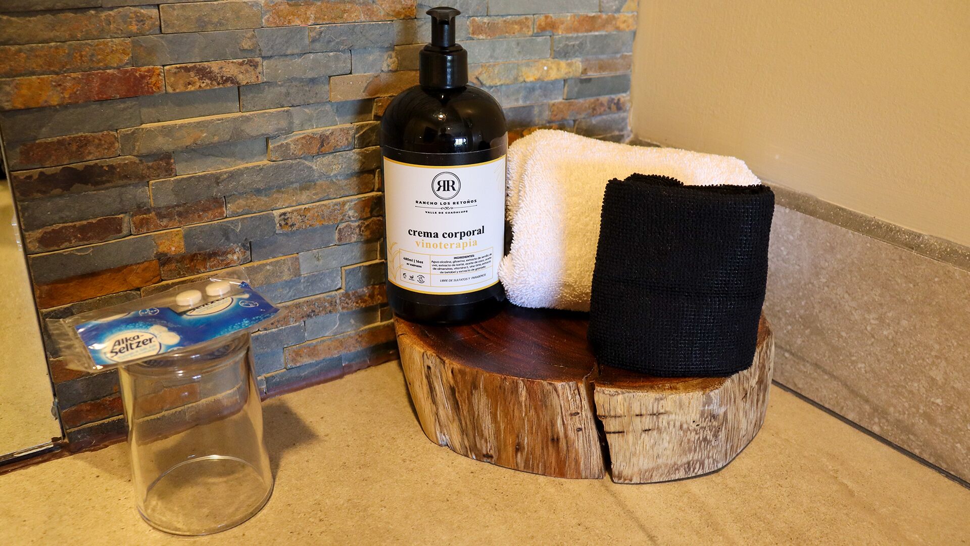 A bottle of Rancho Los Retonés crema corporal vinoterapia, a towel, and a glass on a wooden surface.