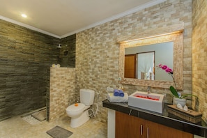A bathroom with a stone wall, a toilet, a sink, and a mirror. - Villa Dion (Canggu)
