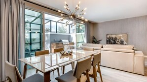 Ein modernes Wohnzimmer mit einem Glastisch, einem beigefarbenen Sofa und einer zeitgemäßen Pendelleuchte.