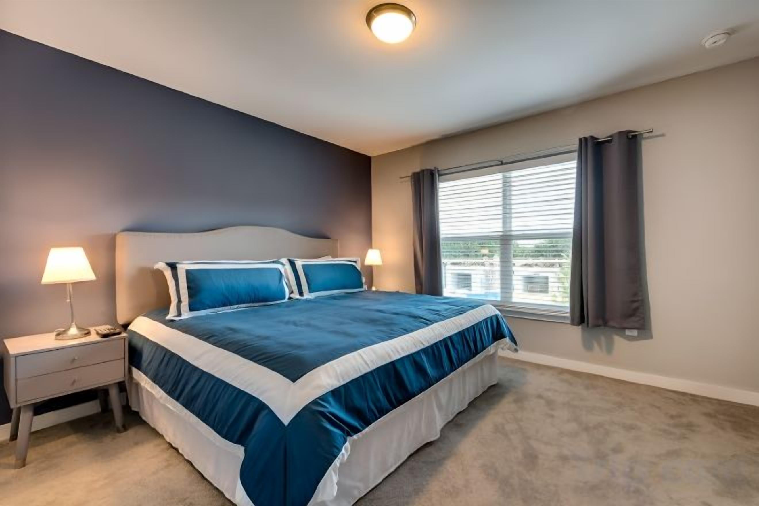 A bedroom with a large bed, a nightstand, a lamp, and a window with curtains.