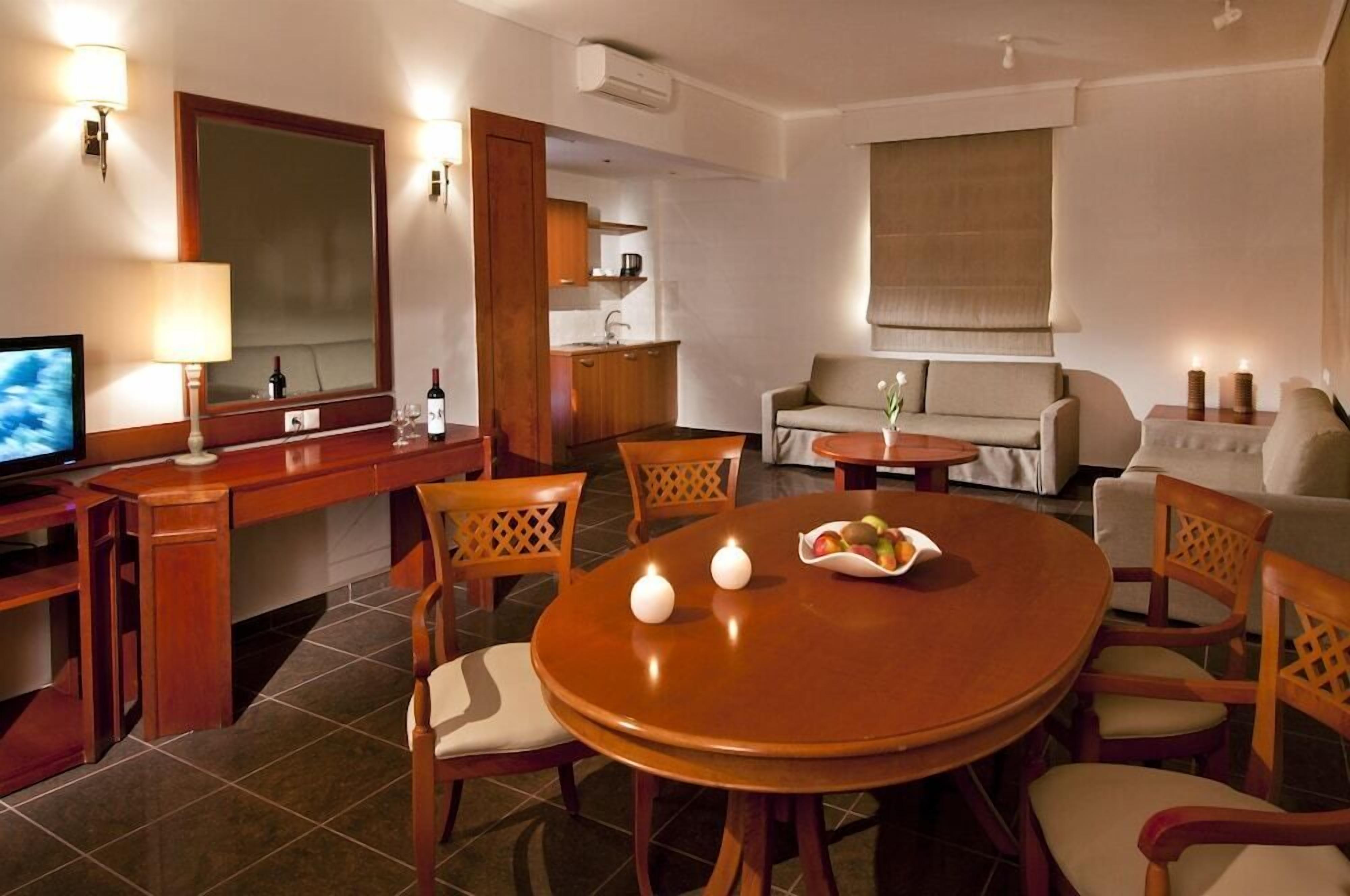 A hotel room with a dining area, a sofa, a TV, and a kitchen area.