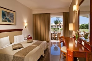 A hotel room with a large bed, a desk, and a view of the outdoor area. - Hotel Kipriotis Village Resort (Kos)