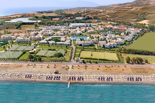 An aerial view of a coastal resort with multiple buildings, a swimming pool, and a beach with umbrellas. - Hotel Kipriotis Village Resort (Kos)
