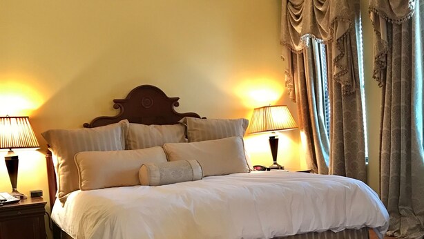 Quarto de hotel com uma cama grande, duas luminárias de cabeceira, um painel de madeira na cabeceira e uma cadeira.