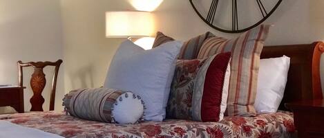 A bed with floral bedding, a clock on the wall, and a lamp in the background.