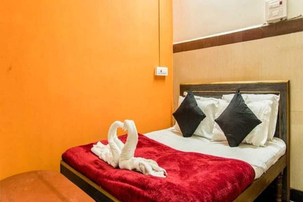 A hotel room with a bed, a red blanket, two black pillows, and a white towel arranged on the bed.