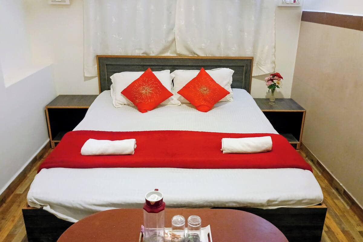 A neatly made bed with red and white bedding, a small table with a tray of toiletries, and a nightstand with a vase of flowers.