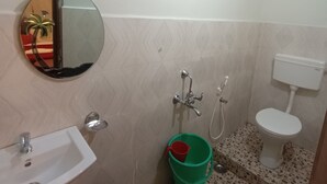 A bathroom with a sink, mirror, toilet, shower, and a green bucket. - Tourist Lodge (Haliyal)