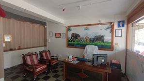 Une salle d'attente avec un sol à carreaux, des chaises en bois, un bureau avec un ordinateur et un tableau représentant des animaux sauvages accroché au mur.