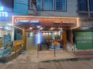 A Tourist Lodge with a sign indicating AC & Non AC rooms, a Travel Desk, and a Tourist Adventures sign. - Tourist Lodge (Haliyal)