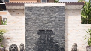 A stone wall with a water feature, flanked by potted plants and decorative statues. - Nashaa Villa (Pattaya)