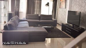 A modern living room with a sectional sofa, a flat-screen TV, and a floor lamp. - Nashaa Villa (Pattaya)