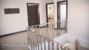 A modern interior with a staircase, a wooden door, and a decorative wall piece. - Nashaa Villa (Pattaya)