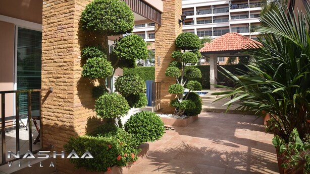 A courtyard with neatly trimmed topiary trees, a pool, and a building with a red-tiled roof. - Nashaa Villa (Pattaya)