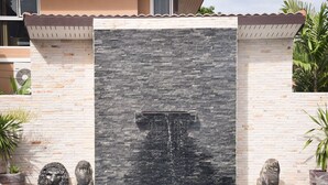 A stone wall with a waterfall feature, a pool with blue tiles, and decorative lion statues. - Nashaa Villa (Pattaya)