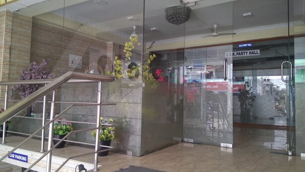 Un área de recepción con una escalera, un vidrio que da al Salón de Fiestas S.S.K., y plantas en macetas.