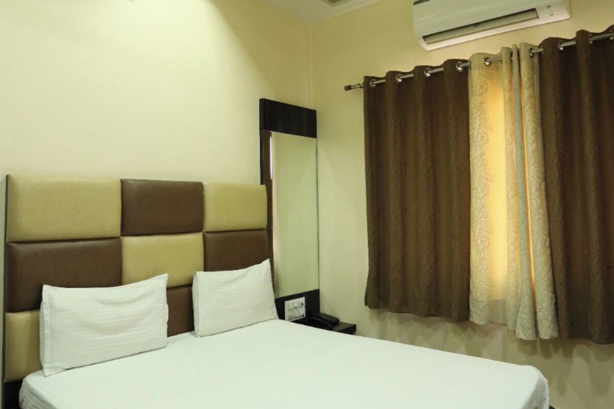 Una habitación de hotel con una cama grande, un ventilador de techo, un equipo de aire acondicionado, un espejo y cortinas.