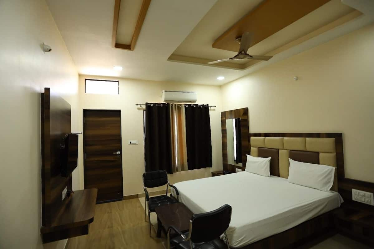 Ein Hotelzimmer mit Bett, Schreibtisch, Stuhl, Fernseher, Klimaanlage und Deckenventilator.