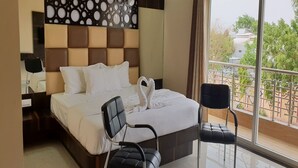 Een hotelkamer met een groot bed, twee stoelen, een decoratief hoofdeinde en een balkon met uitzicht.