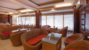A restaurant with wicker furniture, glass tables, and large windows with a view. - Treebo Premium Grand Legacy Elite with Roof Top Cafe (Dehradun)