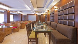 A modern dining area with a long table, cushioned seating, and a high ceiling with recessed lighting. - Treebo Premium Grand Legacy Elite with Roof Top Cafe (Dehradun)