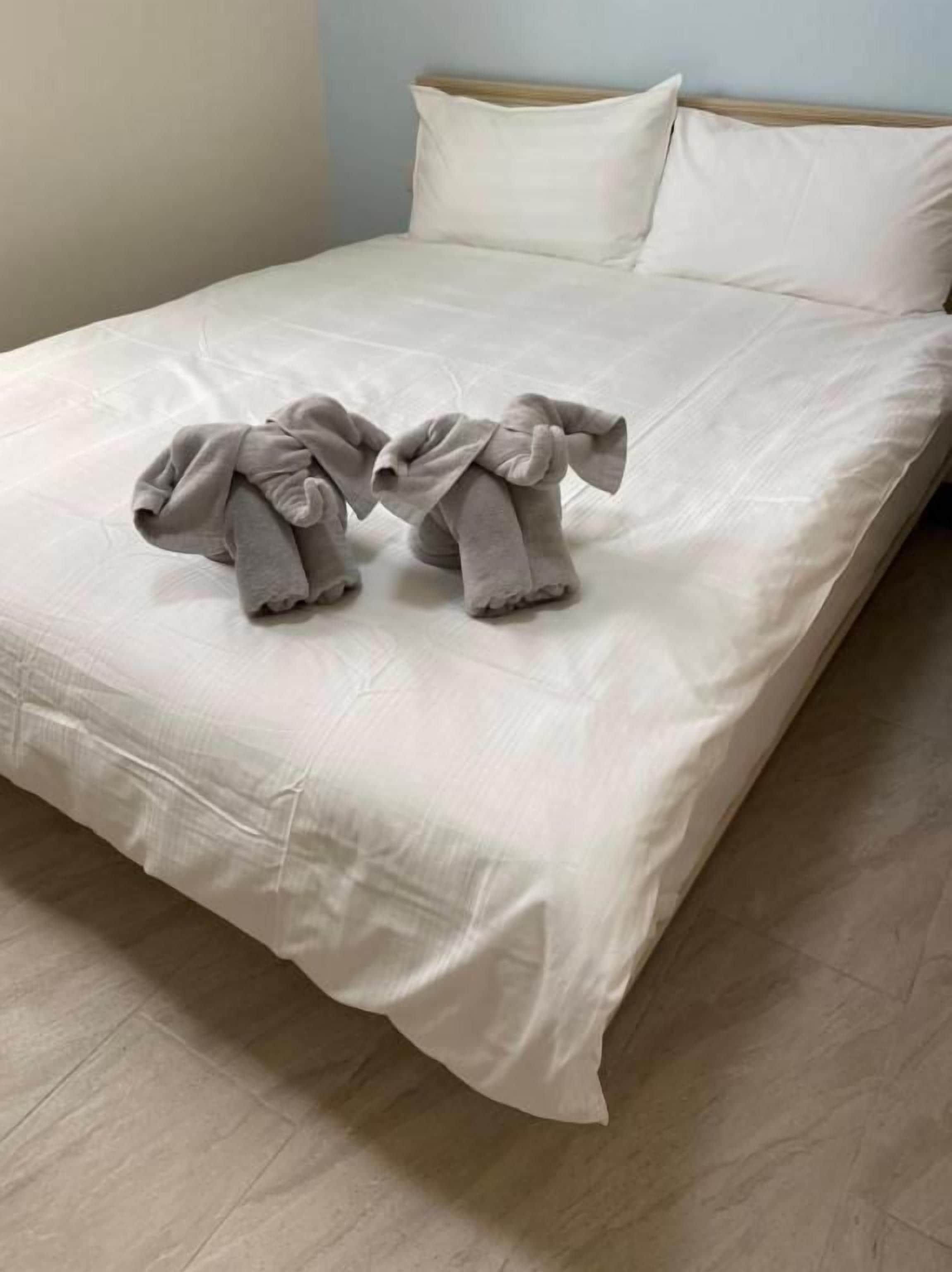 A bed with a white sheet and two towels arranged in a bow shape.