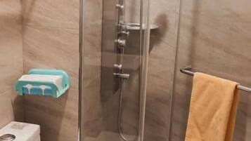 A bathroom with a glass-enclosed shower, a toilet, and a towel rack.
