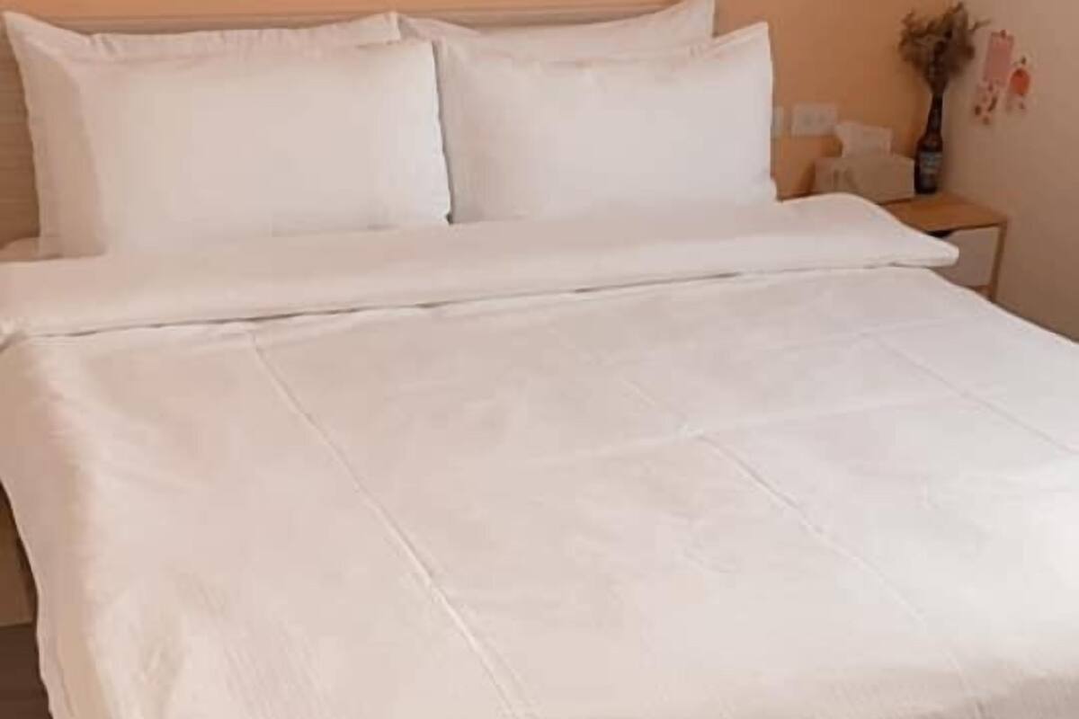 A neatly made bed with white linens in a room with peach walls and a wooden floor.