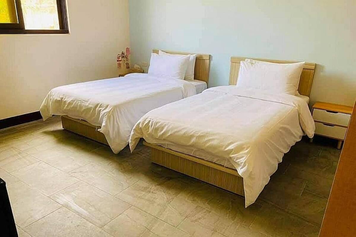 A room with two single beds, a wooden nightstand, and a tiled floor.