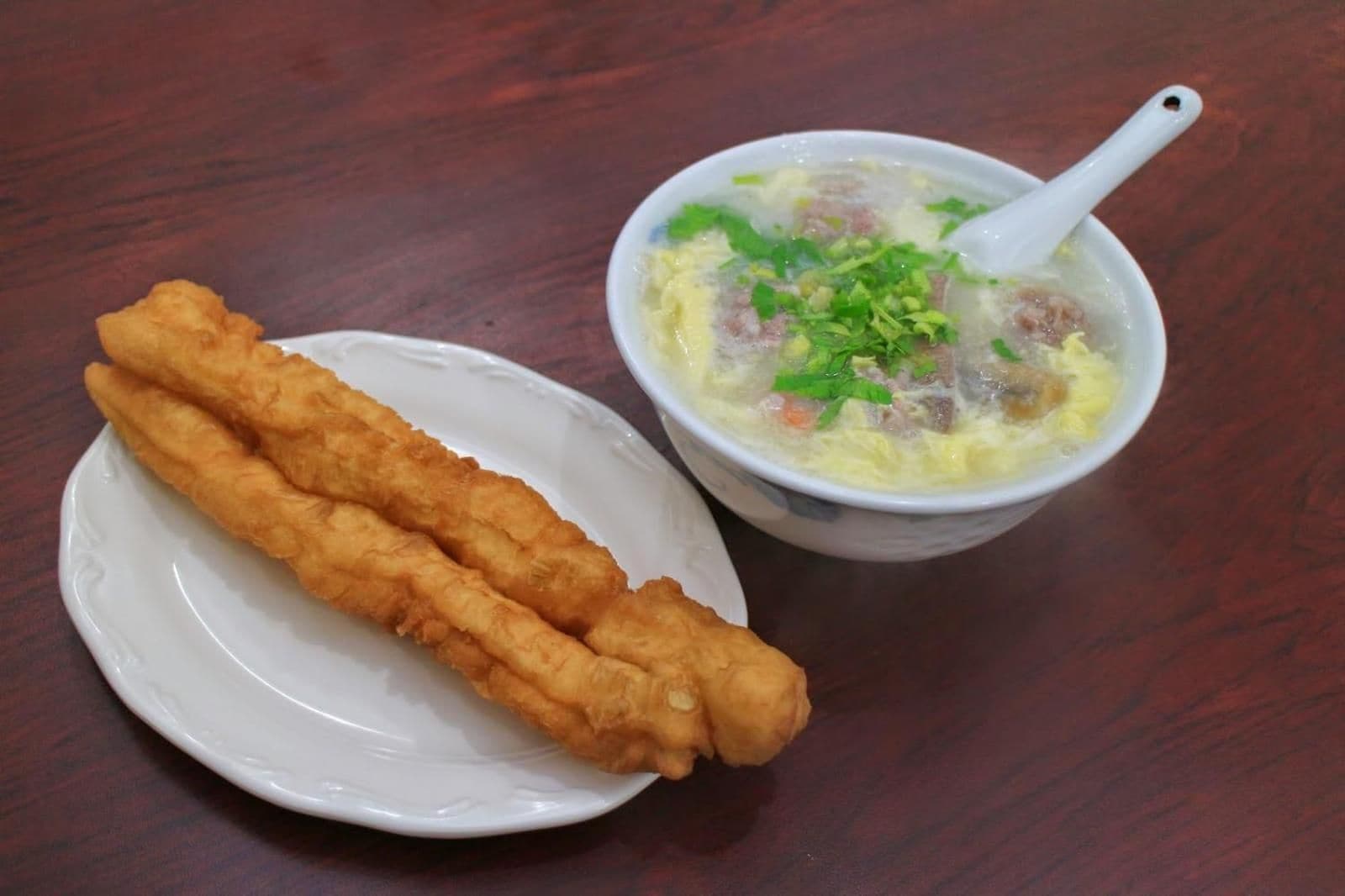 A plate with two fried items and a bowl of soup with a spoon.