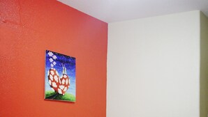 Un lit simple avec une literie blanche et un plaid rouge, un mur rouge et un tableau représentant des cœurs accroché au mur.