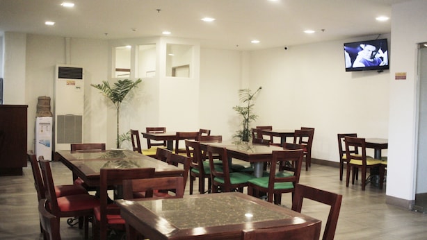 Un espace repas avec plusieurs tables et chaises en bois, un téléviseur fixé au mur et un réfrigérateur dans un coin.